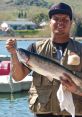 Fisherman proudly holds a large rainbow trout by a scenic lake, showcasing successful fishing trip.