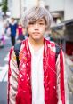 Stylish Japanese youth wearing a red embroidered bomber jacket with light gray hair, captured in a vibrant urban setting.