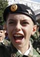 Smiling young boy in military uniform shouting with enthusiasm during a celebration, showcasing Russian military pride.