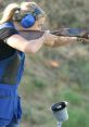 A woman wearing protective gear aims a shotgun on a shooting range, showcasing focus and skill in her stance.