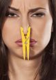 Woman making a funny face with a yellow clothespin on her nose, humorously reacting to unpleasant smells.