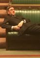 Jacob Rees-Mogg reclining on a green bench in Parliament, capturing a moment of relaxation during a session.