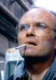 Clarence J. Boddicker from Robocop, smoking with facial scars, portraying a menacing urban character in a gritty environment.