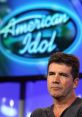 Simon Cowell at an American Idol event, showcasing his iconic serious expression and the show's logo in the background.