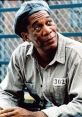 Red from Shawshank Redemption, wearing prison attire, reflects thoughtfully amidst a wire-fenced backdrop.