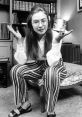 Hillary Rodham Clinton in striped pants and glasses, gesturing thoughtfully in a vintage setting, showcasing her youthful style.