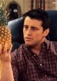 Joey Tribbiani curiously examining a pineapple, showcasing his humorous and iconic personality from Friends.