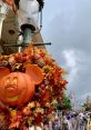 Mickey Mouse pumpkin decoration surrounded by autumn leaves at a festive Halloween celebration in front of a castle.