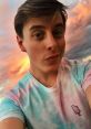 Thomas Sanders takes a playful selfie against a colorful sunset, showcasing his vibrant tie-dye shirt with ice cream design.