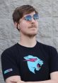 MrBeast wearing sunglasses and a black graphic T-shirt, posing confidently against a textured wall background.