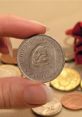 Hand holding a 2015 coin featuring a unique face design, surrounded by various other coins on a surface.