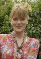 Smiling woman wearing vibrant attire and jewelry, surrounded by lush greenery, embodying the essence of Auntie Angela.