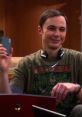 Sheldon smiling and holding his phone while wearing a Green Lantern t-shirt, showcasing his quirky personality and humor.