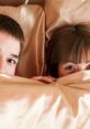 Couple peeking out from beneath soft bedding, capturing a playful and intimate moment of shared closeness.