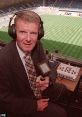 Football commentator wearing headphones in a broadcast booth, ready to provide live analysis during a match.