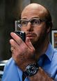 Les Grossman from Tropic Thunder, holding a phone, showcasing his iconic bald look and glasses in a comedic scene.