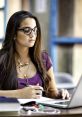 Concentrated female student in glasses working on a laptop, taking notes, showcasing modern learning and technology use.