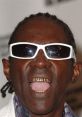 Flavor Flav showcasing his signature style with flashy sunglasses and iconic gold teeth, exuding vibrant energy.