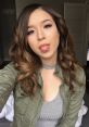 Pokimane poses playfully with a tongue-out expression, wearing a stylish olive green jacket and gray top, showcasing her vibrant style.