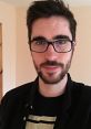 Young man with glasses and a beard, wearing a black jacket. Popular online personality known as Nogla.