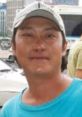 Smiling man in a casual blue shirt and cap, set against an urban background in Vietnam. Friendly local vibe.