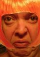 Bold expression with orange wig, embodying the quirky style of TOMAHAWK LADY. Unique and playful facial features.