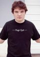 Young man with curly hair wearing a black "Rage Quit" t-shirt, standing confidently against a neutral background.