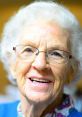 Smiling elderly woman with glasses and white curly hair, embodying warmth and love associated with grandmothers.