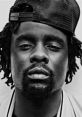 Close-up portrait of Wale, showcasing his signature style with a black cap and intricate dreadlocks.