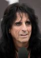 Alice Cooper speaking at a press event, showcasing his signature rock star charisma and iconic long dark hair.