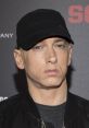 Eminem wearing a black cap and jacket, showcasing his signature style at a promotional event.