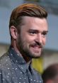 Justin Timberlake smiling during an event, wearing a patterned shirt, showcasing his stylish haircut and facial hair.