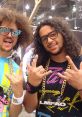 Two performers showcasing LMFAO-inspired fashion and accessories, with energetic poses and vibrant styles.