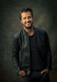 Luke Bryan smiling in a black leather jacket, showcasing his signature style and charisma against a muted background.