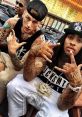 Machine Gun Kelly and Waka Flocka pose with tattoos and hand signs, showcasing their unique styles and hip-hop culture.