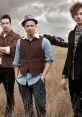 OneRepublic band members posing outdoors in a field, showcasing their unique style and artistic presence.