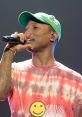 Pharrell Williams performing live, wearing a colorful tie-dye shirt and green cap, captivating the audience with his energy.