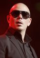 Pitbull performs on stage wearing sunglasses and a black suit, exuding confidence and energy under vibrant lighting.