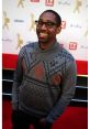 PJ Morton smiling at a red carpet event, wearing a stylish sweater, showcasing his engaging personality and fashion sense.