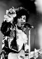 Prince performing passionately on stage with a mic, wearing a stylish black and white outfit, captivating the audience.