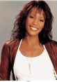 Whitney Houston smiling confidently, showcasing her style with a brown jacket and layered jewelry against a neutral background.