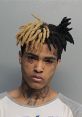 Mugshot of XXXTentacion with unique two-tone dreadlocks and visible tattoos, reflecting his controversial public image.