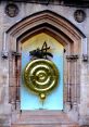 Golden Cambridge clock in archway, showcasing intricate design and craftsmanship, surrounded by historical stonework.