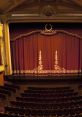 Elegant theatre stage with rich red curtains and ornate details, showcasing a classic performance space and audience seating.