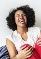 Joyful woman with curly hair laughing heartily, radiating happiness in a casual setting, showcasing the power of laughter.