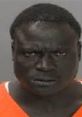 Mugshot of an irate Black man wearing an orange prison jumpsuit, displaying intense facial expressions.