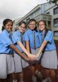 Four girls in blue school uniforms demonstrating friendship and teamwork outside a secondary school on a sunny day.