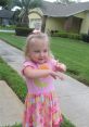 Toddler girl, 2-3 years, in a colorful dress, playing outdoors on a sunny day with a joyful expression.