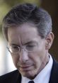 Man in a suit with glasses, looking down, reflecting serious thoughts or emotions in a contemplative moment.