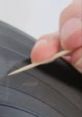 Hand using a toothpick to inspect tire tread for wear and safety, ensuring optimal vehicle performance and safety on the road.